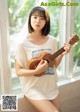 A young woman holding a ukulele in front of a window.